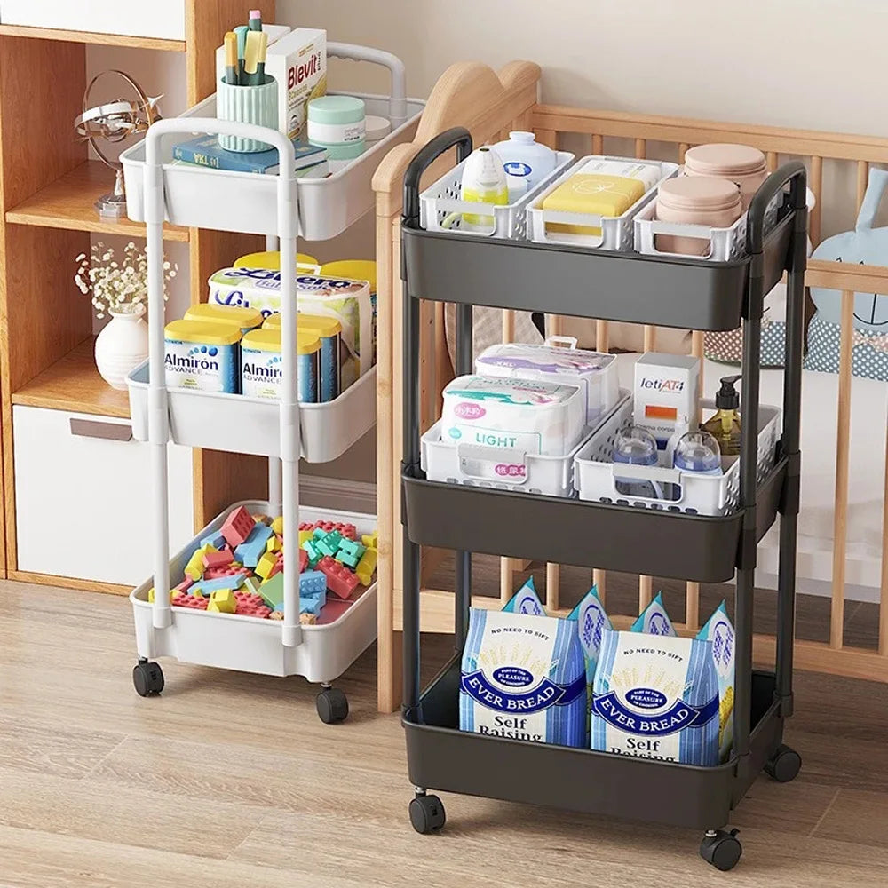 Chariots de rangement blanc et noir à 3 niveaux, placés dans une pièce avec lit bébé – remplis de produits alimentaires, soins pour bébé et accessoires du quotidien. Rangement pratique et mobile pour jeunes parents.