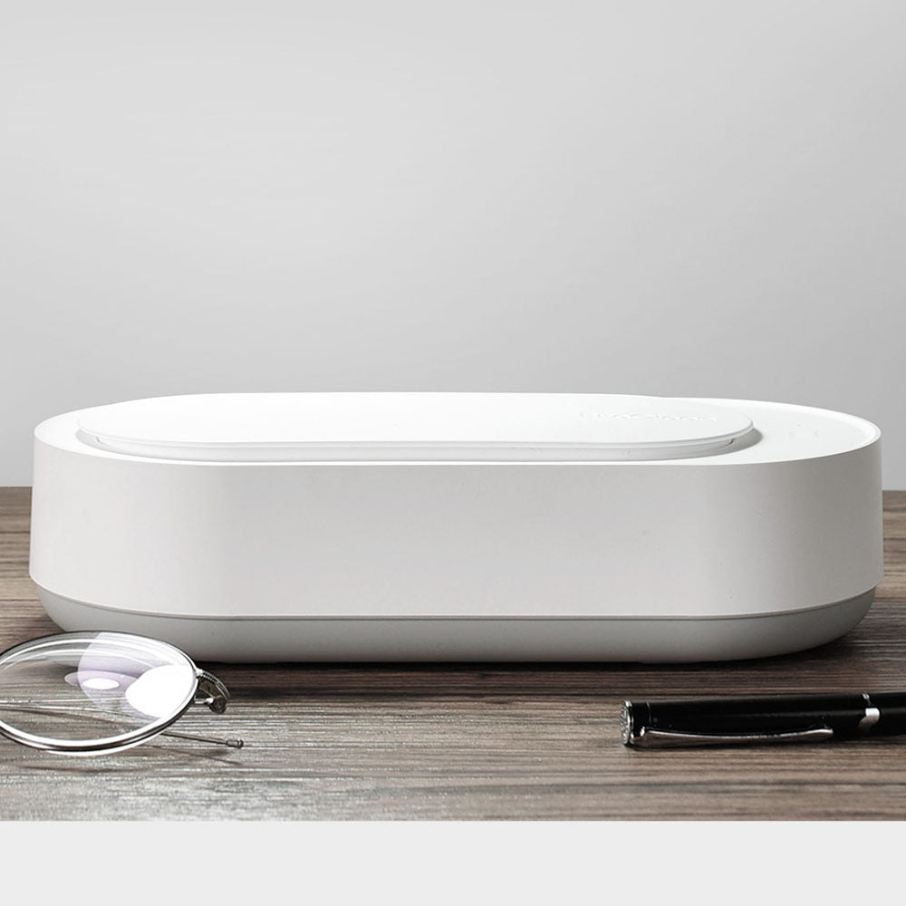 Nettoyeur ultrasonique portable 45000Hz blanc posé sur une table en bois, accompagné de lunettes et d’un stylo, mettant en avant son design sobre et épuré.