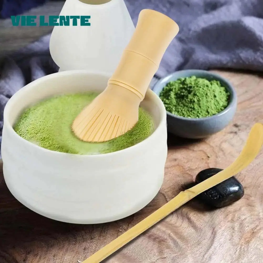Fouet à matcha moderne dans un bol blanc rempli de thé matcha mousseux, avec poudre verte et cuillère traditionnelle en fond