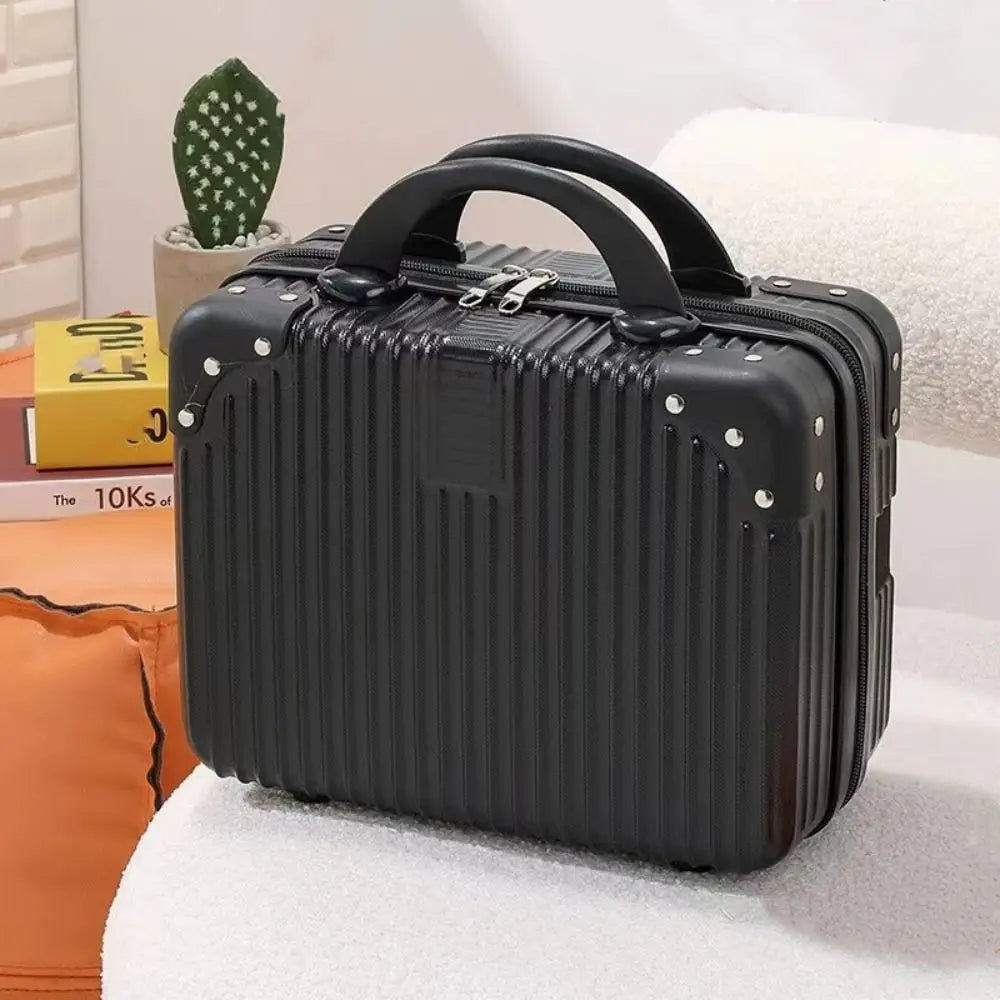 Mini valise rigide noire posée sur un canapé blanc, avec double poignée et coins renforcés, idéale pour les voyages ou le rangement d’accessoires
