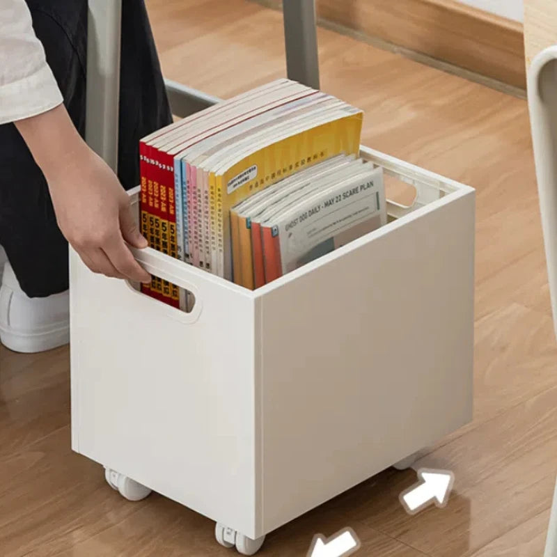 Personne saisissant une boîte de rangement blanche à roulettes remplie de livres – rangement mobile et pratique pour optimiser un coin bureau ou une chambre.