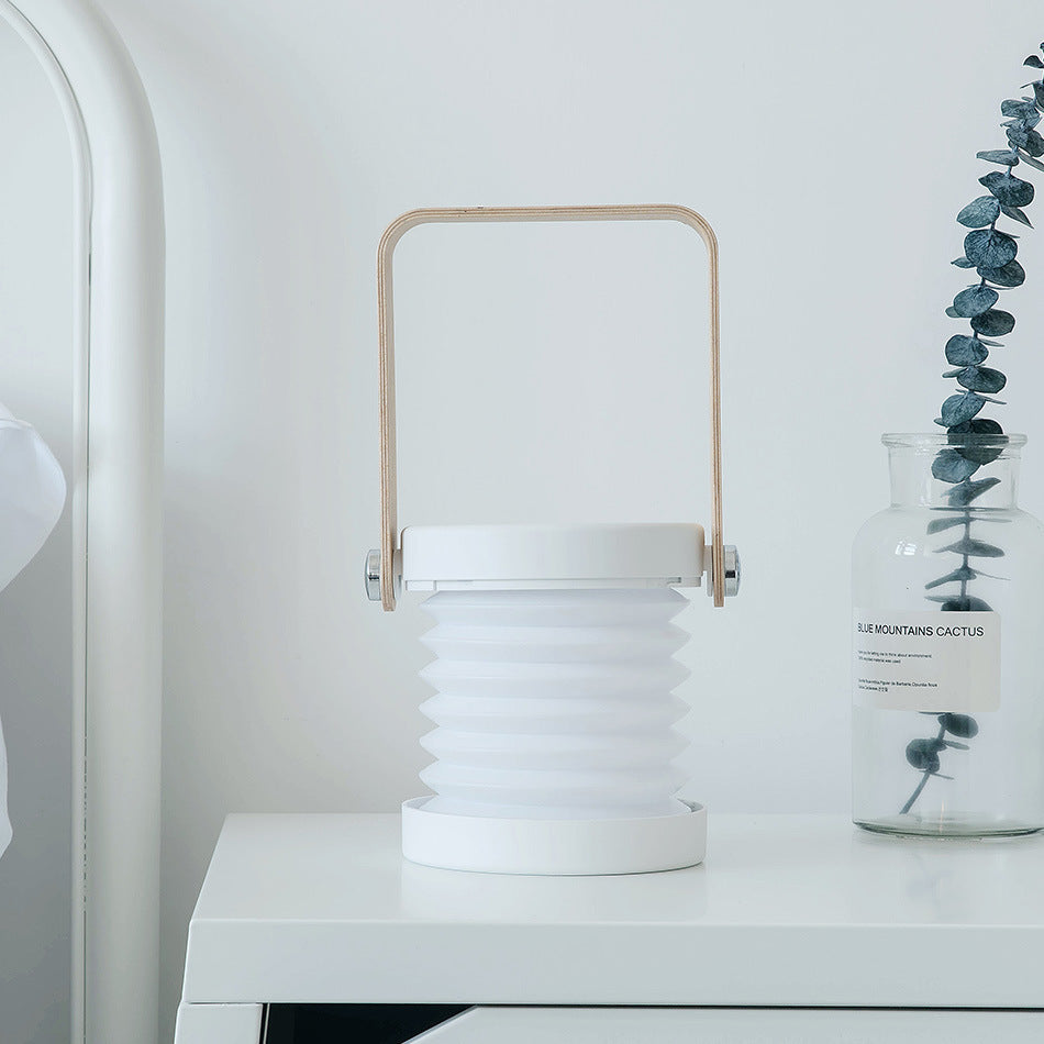Lampe LED nomade blanche posée sur une table dans un intérieur minimaliste – design pliable avec poignée bois, idéale en veilleuse ou lampe d’ambiance.