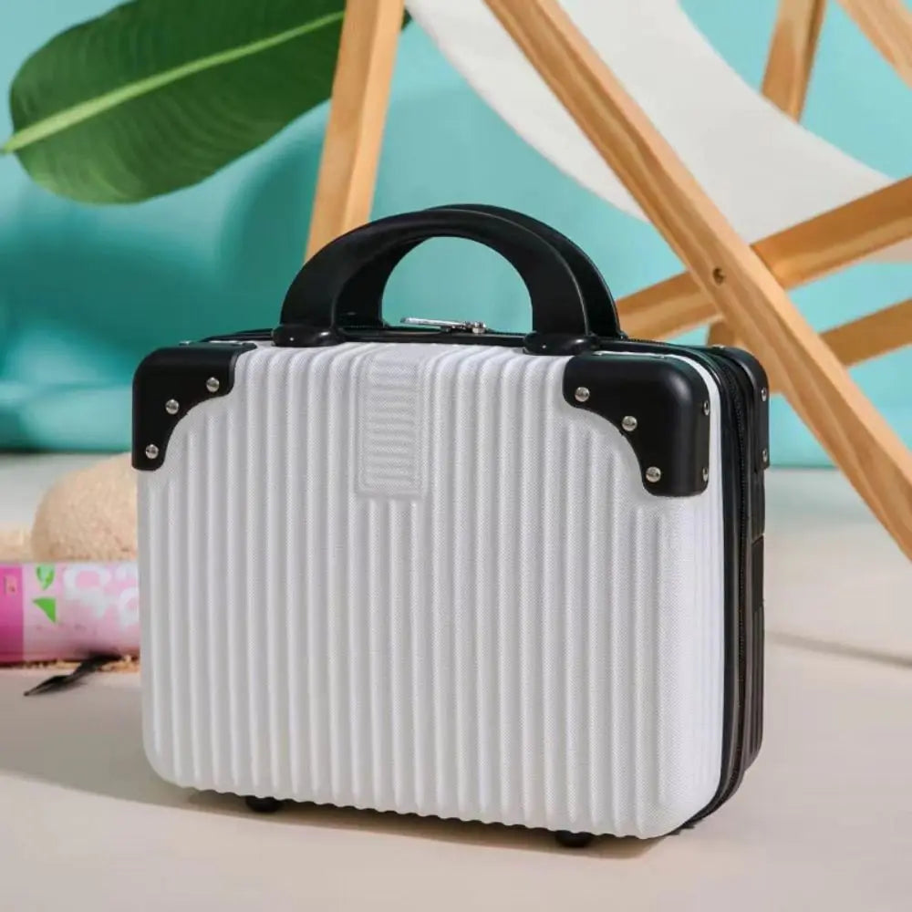 Mini valise rigide blanche avec coins noirs renforcés, posée sur une table avec décor tropical, idéale pour les accessoires ou le maquillage en voyage