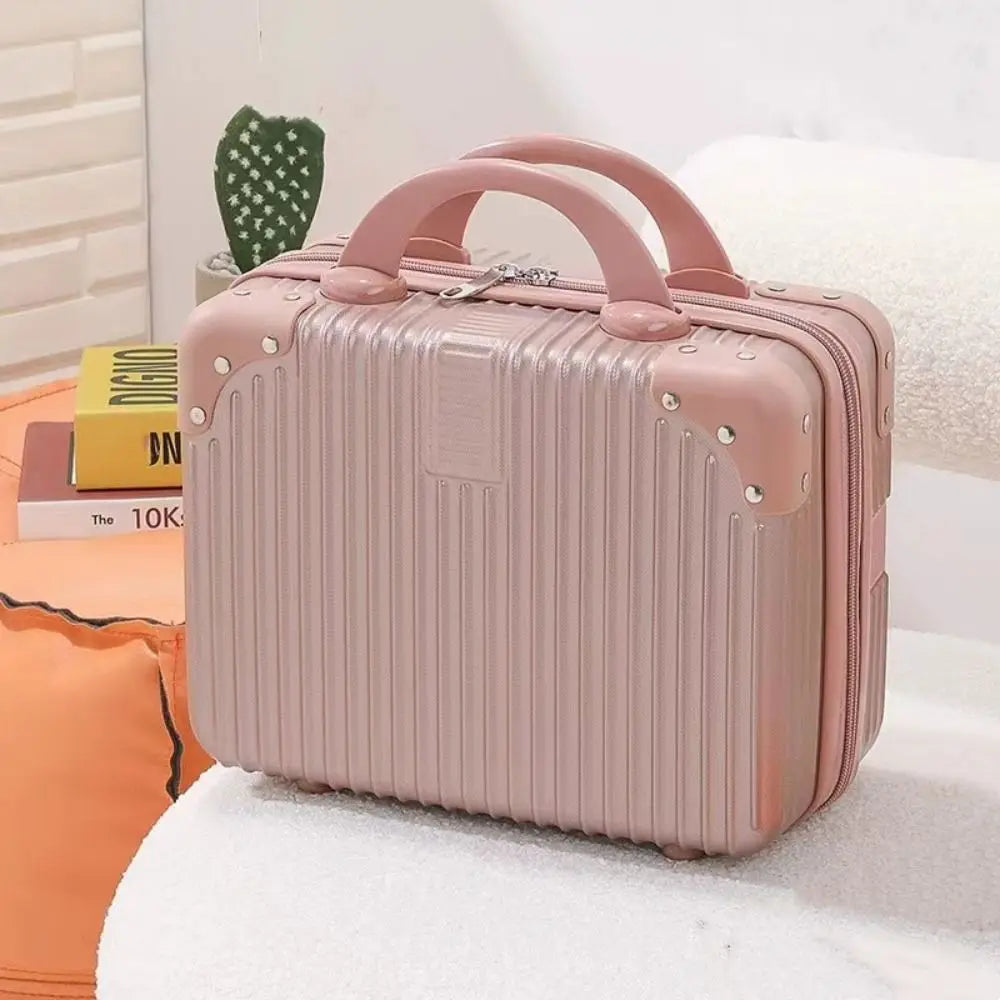 Mini valise rigide rose posée sur un canapé blanc, avec livres en arrière-plan, idéale comme trousse de voyage ou rangement beauté élégant