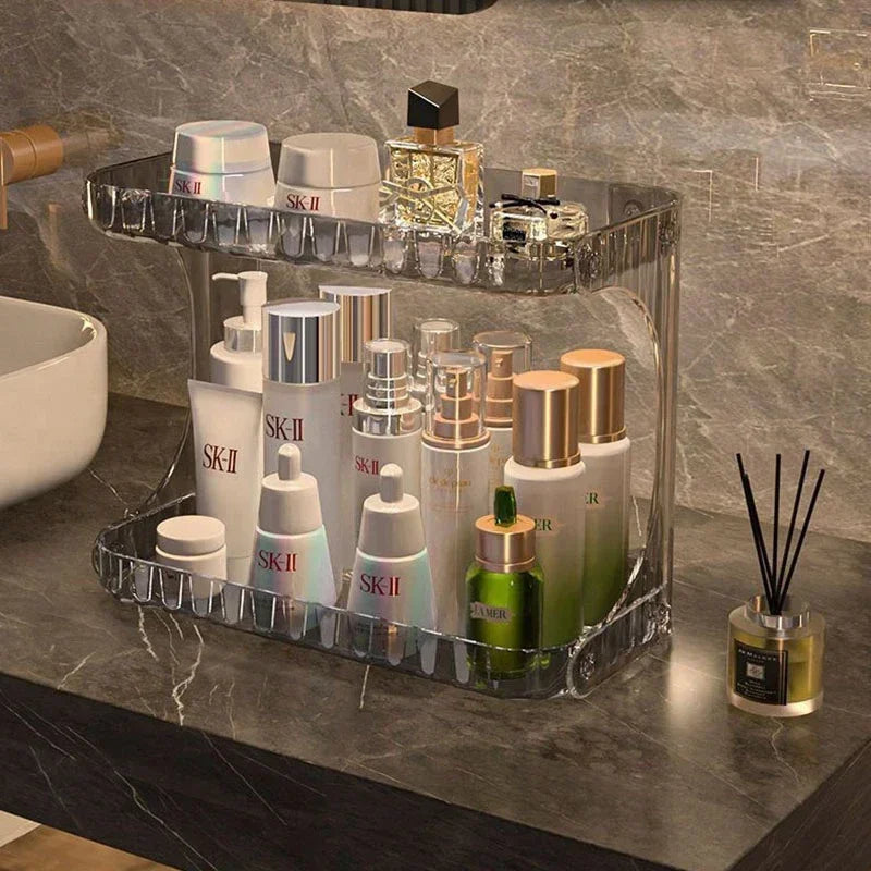 Organisateur de cosmétiques en acrylique transparent à deux étages, exposant des soins de peau, sérums et parfums de luxe sur un plan de salle de bain élégant effet marbre.